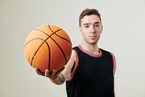 Handsome young serious Caucasian basketball player outstretching arm with ball and 