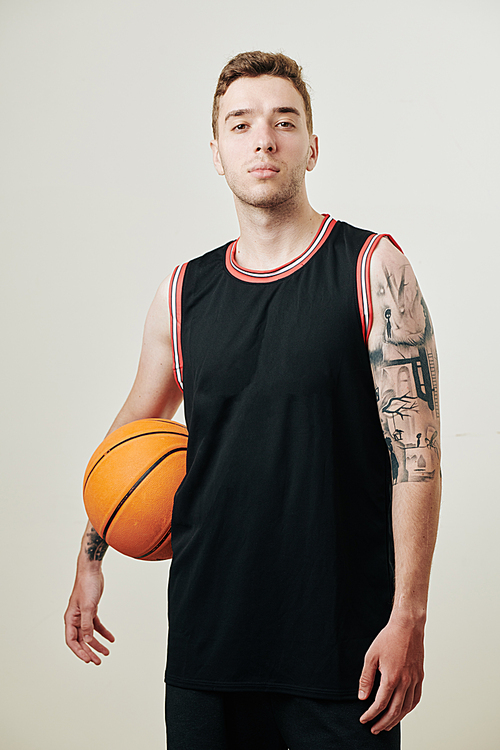 Confident serious backetball player in black uniform holding ball and , isolated on white