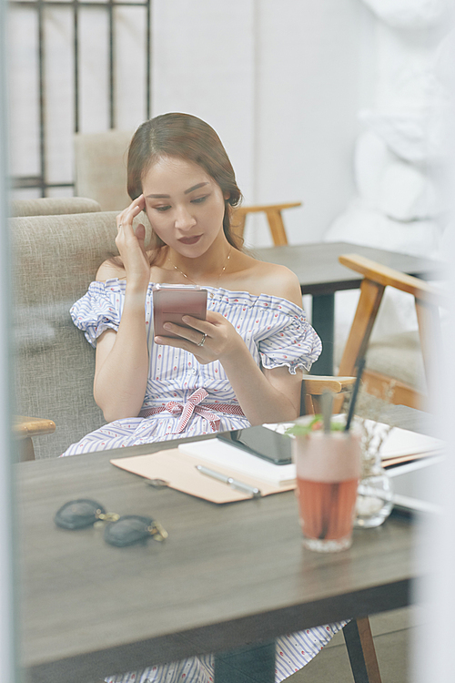 Serious young Vietnamese woman trying to concentrate when reading text message on smartphone