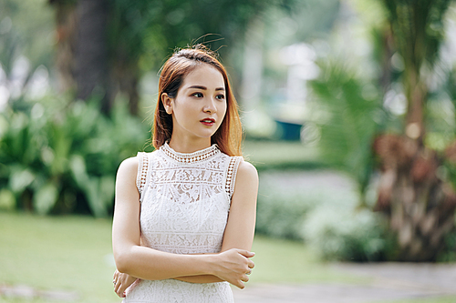Portrait of young beautiful Vietnamese woman in white lace dress standing outdoors