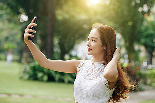 Beautiful young Vietnamese woman taking selfie on smartphone when walking in park