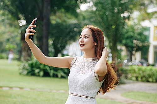 Pretty lovely Asian girl with long hair smiling and posing for selfie in park