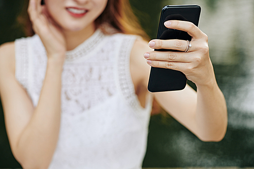 Close-up image of smiling young woman taking selfie on smartphone, selective focus
