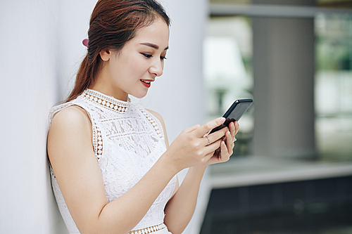 Pretty young smiling Asian woman reading text message from boyfriend