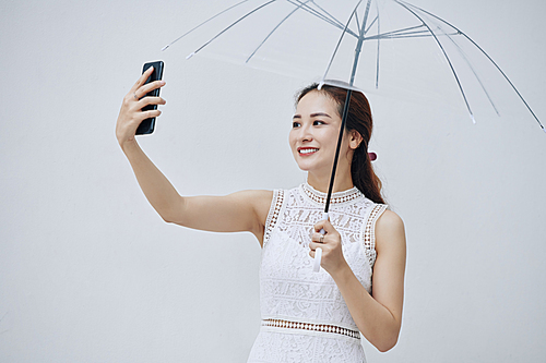 Pretty young Asian woman smiling when talking selfie with transparent umbrella