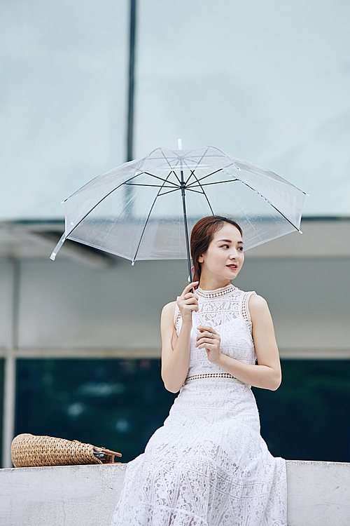Lovely young Asian woman resting outdoors with umbrella in hand