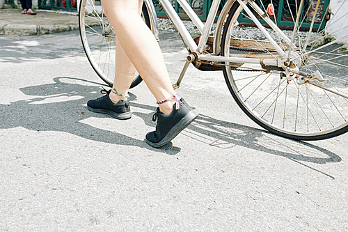 Legs of young woman with feet bracelets walking in street with her bicycle
