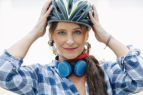 Portrait of smiling pretty woman with headphones around her neck putting on helmet