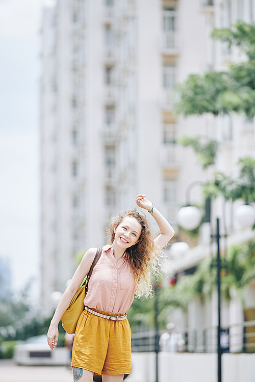 Happy young woman with blond curly woman standing on the street on big city and smiling at camera