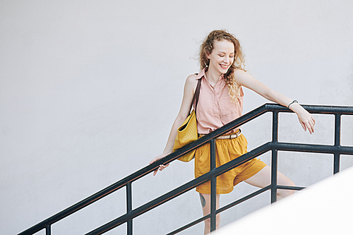 Happy laughing pretty girl leaning on railing and looking down from the staircase