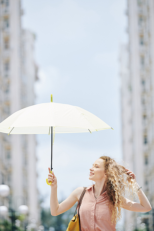 Happy yuong woman walking in the street with white parasol on beautiful summer day