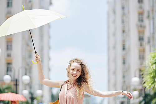 Happy young pretty woman walking in the street with umbrella in hand on windy day