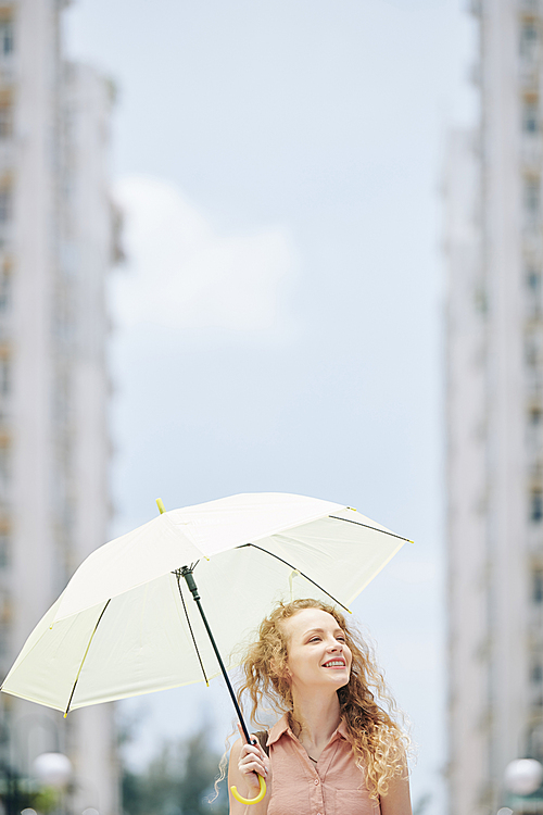 Beautiful young Caucasian woman with big white umbrella walking in city
