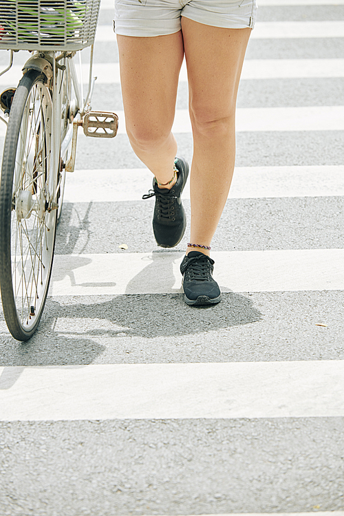 Fit legs on young woman walking next to her bicycle when crossing road in city