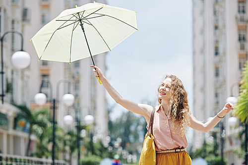 Pretty curly young woman using umbrella to protect herself from shining sun