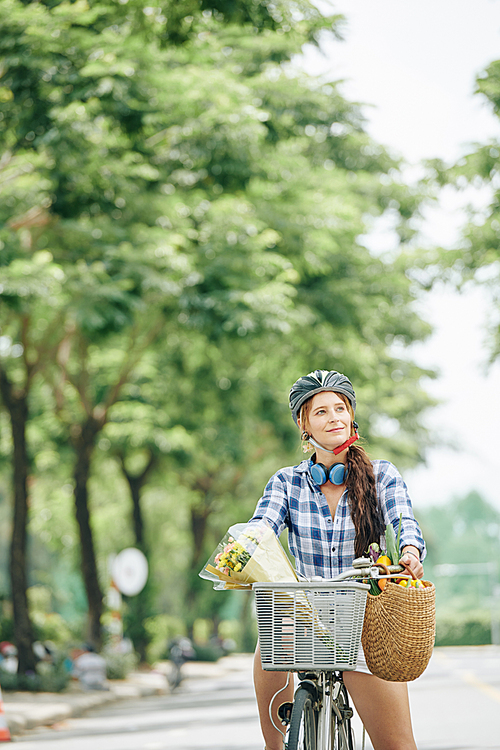 Portrait of cheerful young woman wearing helmet when riding bicycle in city street on summer day