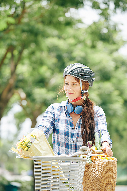 Portrait of cheerful smiling young woman riding bicycle with bouquet of flowers in basket