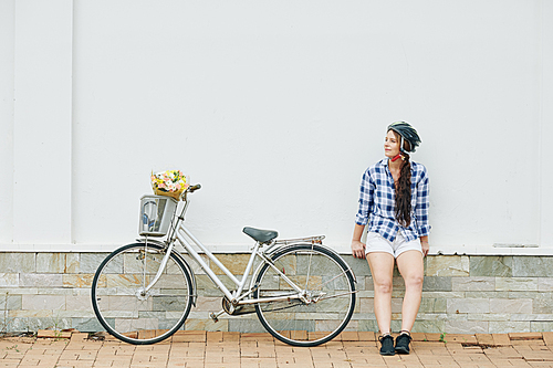 Young active woman sitting outdoors after riding bicycle in the city and pondering over her day