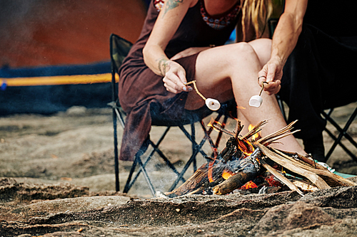 Cropped image of travelers using sticks when frying marshmallows on fire