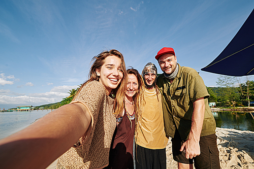Group of young people smiling and posing for selfie after walking on the beach