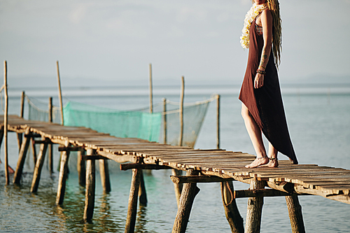 Cropped image of barefoot woman in cotton dress walking on narrow handmade wooden pier