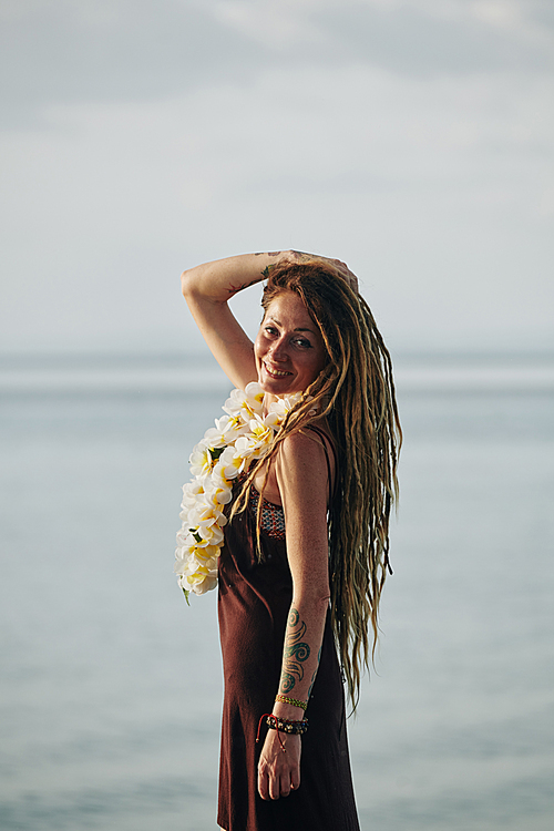 Portrait of smiling beautiful woman with dreadlocks posing with flower necklace against calm sea