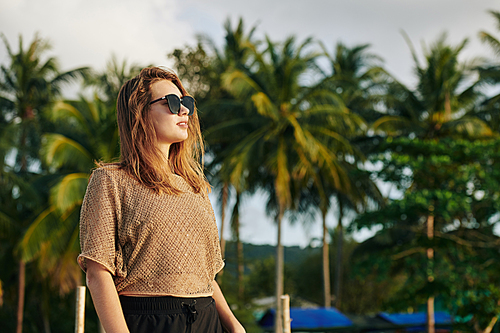 Pretty young woman in sunglasses walking on beach and enjoying beautiful sunset