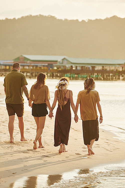 Group of friends holding hands when walking on sea beach in sunset sun rays