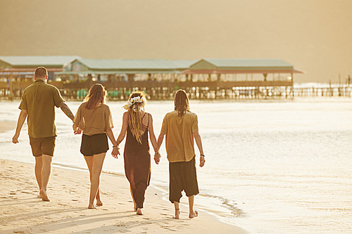 Two couples holding hands when enjoying walking on beach during sunset when sun rays reflecting off water