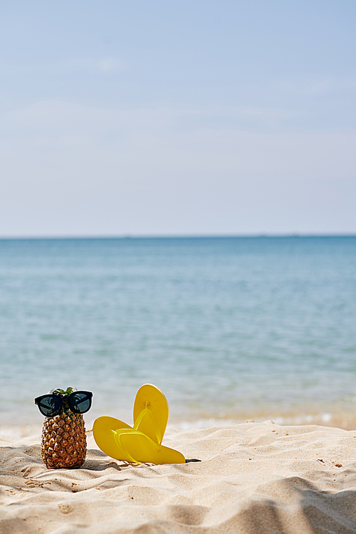 Flip-flops and pineapple with sunglasses on it on sandy beach on island