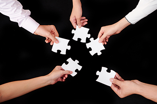 Close-up of business people holding pieces of puzzles and trying to connect them over black background