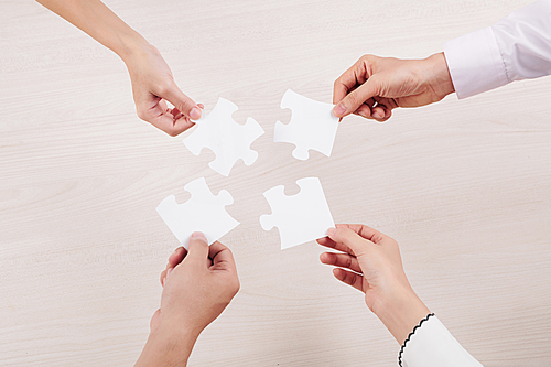 Close-up of group of people holding pieces of puzzles and connecting them with each other over white background