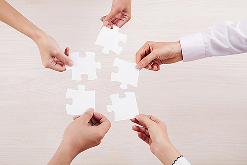 Close-up of team connecting their puzzles and demonstrating unity of friendship isolated on white