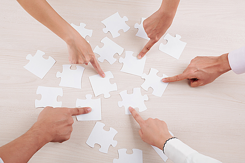 Close-up of group of people pointing at pieces of puzzles and collecting them together in team