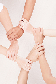 Close-up of group of young people holding hands and making chain from their hands over white background