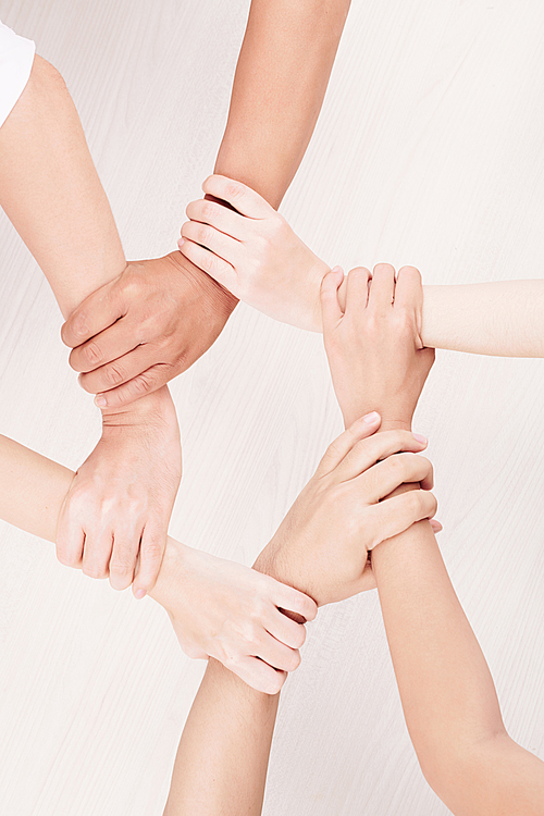 Close-up of group of young people holding hands and making chain from their hands over white background
