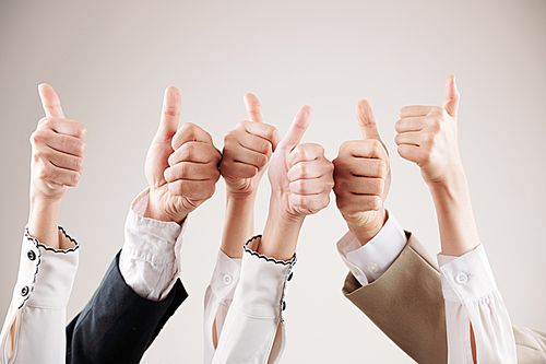 Close-up of group of business people raising their arms up and showing thumbs up isolated on white