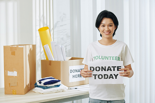 Portrait of pretty smiling young Asian volunteer with donate today placard