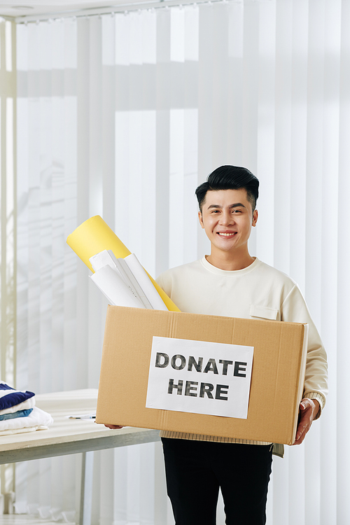 Portrait of happy young Vietnamese volunteer holding cardboard box for donations