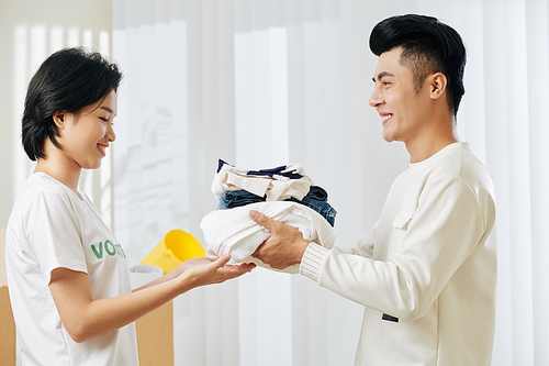 Handsome smiling young Asian man donating his old clothes in volunteer center