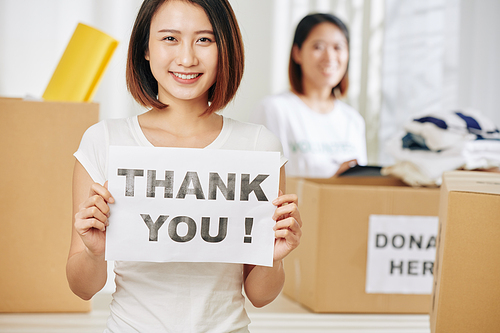 Lovely pretty young Asian woman with thank you placard in hands working at donation center