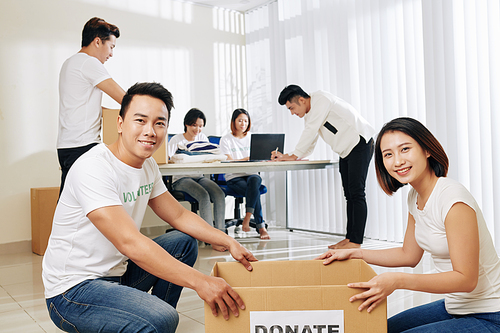 Workflow in donation center: young couple packing donated clothes when their colleague working with documents in background