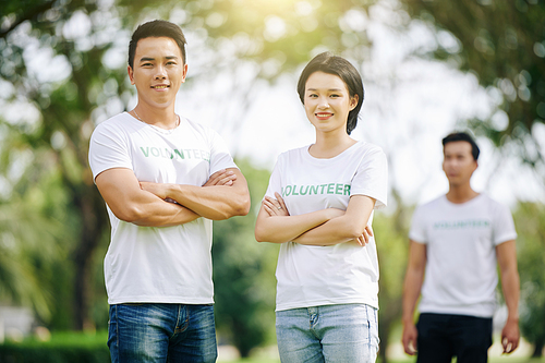 Young Asian volunteering stundents standing in park with arms folded and smiling at camera