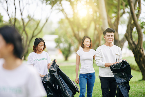 Group of young smiling Asian volunteers collecting garbage in city park