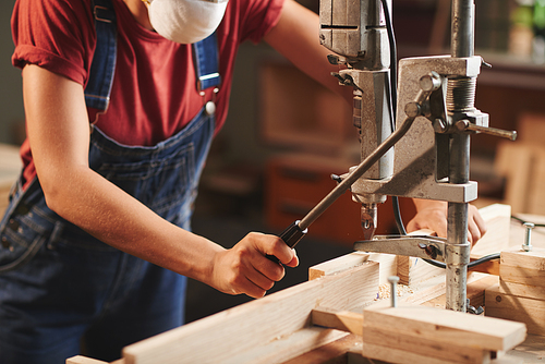 At manufacturing workshop. Close-up view of female carpenter in denim overall pressing lever on woodworking machine while processing wooden planks