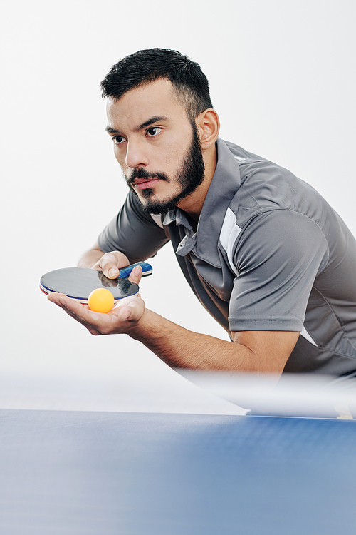 Serious Hispanic sportsman getting ready to serve the ball and start a game of table tennis