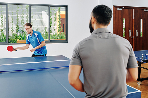 Young men in sports clothing enjoying playing table tennis in office lounge room