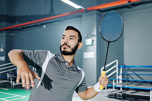 Professional Hispanic badminton player hitting shuttlecock when playing in gymnasium