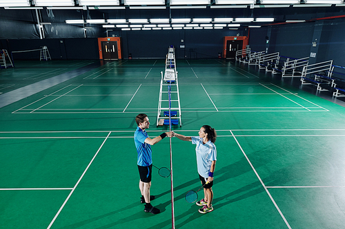 Young male and female badminton players shaking hands after training in gymnasium