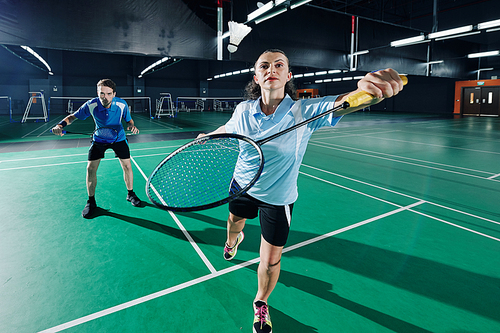 Concentrated couple playing badminton in team in gymnasium